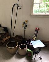 Wide view of planters, garden hooks, decorative peony flower stakes, hummingbird feeder box, and some garden supplies near a window.