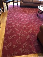 Red area rug with beige leaf patterns on floor next to furniture.