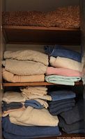 Folded assortment of towels stacked on wooden shelves including beige, blue, pink, and brown colored towels