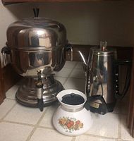Farberware coffee urn, Universal GE coffee pot, and Corning Ware teapot on tiled surface