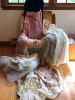Overview of four vintage gowns draped over and around a storage box, showing white tiered tulle gown, blush-peach chiffon gown, peach satin dress and white chiffon sequin gown