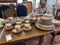 Wide view of the china set with many teacups, saucers, plates, cream and sugar bowl on wooden table, showing the overall set quantity and arrangement.