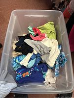 Top view of bin filled with assorted children's clothing including colorful t-shirts and shorts