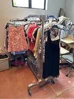 Full side view of metal clothing rack with clothes hanging, wheels visible on base, showing overall design and condition.