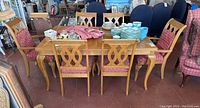 Full view of the dining table with six matching cushioned chairs and dishes placed on the table, showing overall condition and design.
