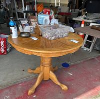 Full view of round oak pedestal dining table with star pattern tabletop, displayed in a garage setting with various items on the table.