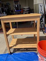 Front view of the wooden kitchen cart showing three shelves, top surface and one caster wheel.
