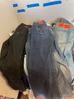 Multiple pairs of women's designer jeans stacked together, showing various washes, styles, and brand tags.