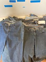 Overall view of ladies jeans folded and stacked by size with visible size labels 9, 10-12 and 30, showing different colors of denim.