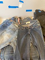 Several pairs of ladies denim jeans with different washes, casually stacked, showcasing variety in color and size.