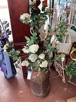 Photo showing full vintage milk can with artificial white roses inside on floor next to furniture and other decor items