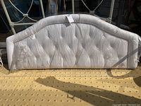 Front view showing the upholstered tufted queen-sized headboard with curved top edge and light-colored fabric.