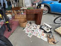 Wide shot of sewing machine cabinet, black Singer Stretch Stitch machine with foot pedal, sewing basket and many vintage sewing patterns spread out on ground.
