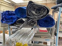 Top view showing six rolled tarps in blue and black colors stacked on a shelf.