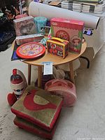 Full view of round wooden table topped with various items including Spiderman lunchbox, Strawberry Shortcake clock box, photo album, water cups, foot stools, and toys.