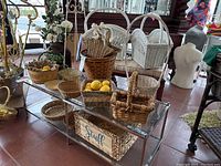 Variety of woven and wicker baskets in natural and white finishes displayed on glass shelving with decorative items around