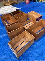 Eight wooden crates displayed on blue tarp, showing different shapes and sizes. One crate with 'Pears' label visible.