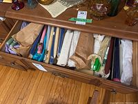 Drawer view showing multiple bundles of taper candles mostly wrapped in paper and some in plastic with visible blue, pink, cream, and green candles.
