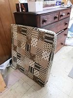 Folded card table with patterned, padded fabric cover in front of a wooden dresser in basement.