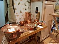 Full view of copper set including jug, molds, and serving pieces on a wooden shelf.