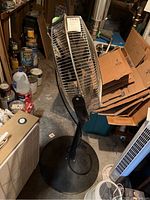 Pedestal fan approx 48 inches tall, black metal stand, circular base, metal grille protecting blades.