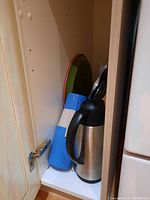 Kitchenware items stored inside a cabinet showing thermos, measuring cups, trays, and stand.