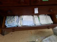 Drawer filled with folded linens, including pillow covers and bed sheets in various light colors and patterns.