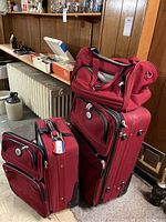 Three piece luggage set: two wheeled suitcases and one carry-on tote bag, all in red fabric.
