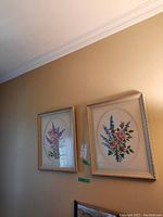 Two framed needlepoint floral artworks hung on wall, showing overall appearance and size relative to room.