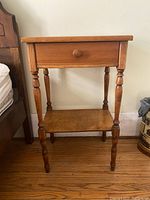 Side view of wooden nightstand next to a bed showing the turned legs and shelf.