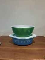 Two stacked Pyrex bowls - green mixing bowl on top, blue casserole bowl with white lid and blue floral pattern underneath.