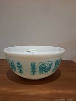 Side view of large Pyrex bowl with blue roosters, corn stalks, and farming pattern, including lid on top.