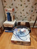 Lot overview showing stacked boxes including a blue vacuum carafe and boxed kitchenware; Aspen blue glass serving bowl with lid on top of a box