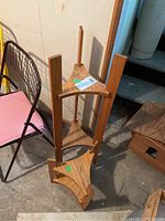 Pair of wooden shelves or plant stands stacked upside down, showing triangular tops with three legs each, natural wood finish with some wear.