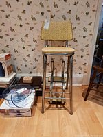 Front view of the vintage step stool showing metal frame and yellow vinyl seat and backrest.