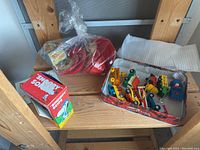 Shelf view of lot with bagged plastic children’s bowls and cups, metal tray with small toy cars, and boxed Snoopy soap.