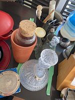 Photo showing terracotta wine cooler, glass decanter with stopper and metal label chain, metallic container with bar tools.