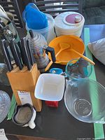 Photo showing coffee pot, salad bowl with servers, storage containers, glass measuring cups, knife block with knives, and ceramic cream pitcher on table.