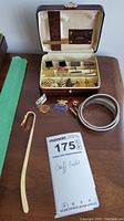 Overall view of cufflinks, pins, tie clip, bookmark, and bracelets arranged on table and inside display case