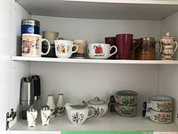 Complete lot of coffee cups, cream and sugar set, salt and pepper shakers, and bowls arranged on shelves.
