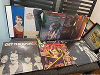 Seven vinyl record covers displayed on a couch featuring various artists and styles.