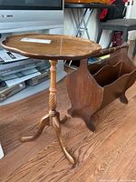 Full view of wooden side table with scalloped top and carved pedestal base, next to magazine rack