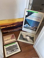 Five framed photos arranged on floor and leaning against wall, showing vintage and modern styles with landscape and artistic themes.