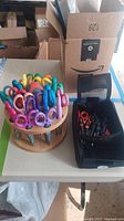 Wooden caddy filled with colorful crafting scissors and black carrying case with scissors inside on table