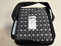 Closed tote bag with black and white floral pattern and black strap. Shows lot label.