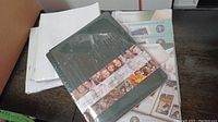 Photo of Creative Memories Tribute Album and stacked unopened page protector sets on a dark wood surface.