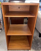 Front view of the wood entertainment center showing three shelves and a cable management hole in the back panel.