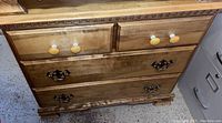 Front view of wood dresser showing four drawers with different hardware knobs and handles.
