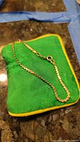 Seven inch serpentine gold chain placed on green cloth showing clasp and link details.