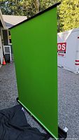 Front view of the green screen fully extended vertically outdoors on a gravel surface.